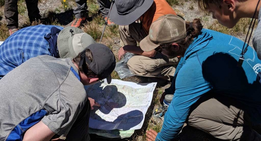 students gather around a map on the ground during a backpacking course with outward bound